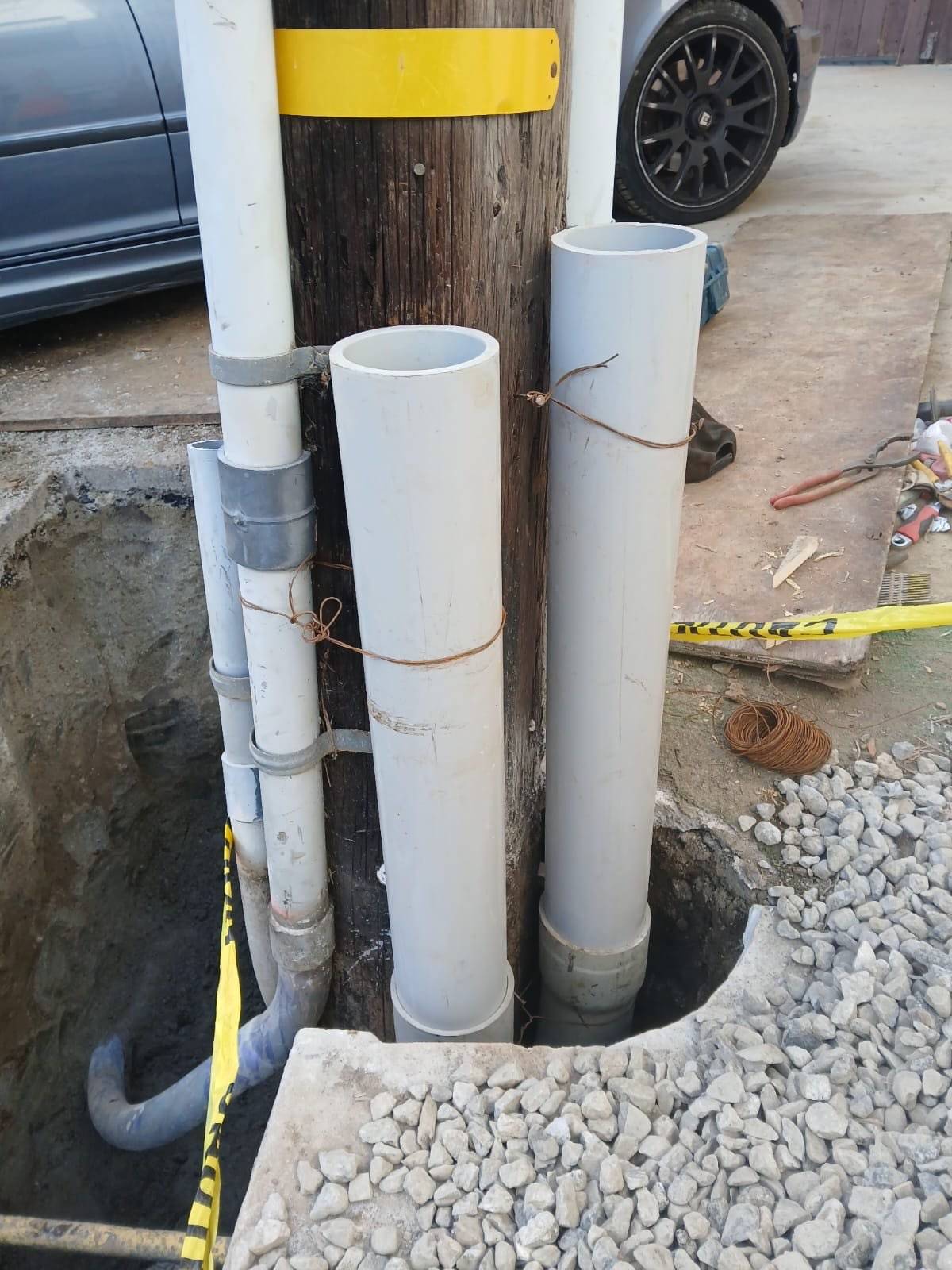 PVC risers strapped to a wood utility pole above an open pit